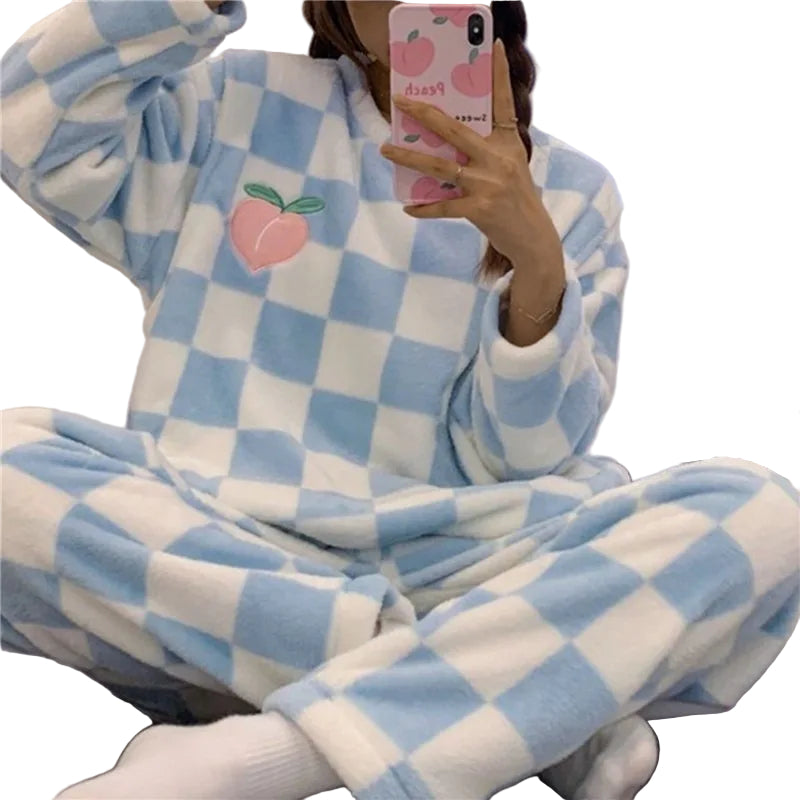 Femme portant un pyjama chaud à carreaux bleu ciel et blanc, avec un motif pêche brodé sur le haut. Ensemble à manches longues et pantalon assorti, doux et confortable, parfait pour les soirées d’hiver ou le cocooning à la maison.