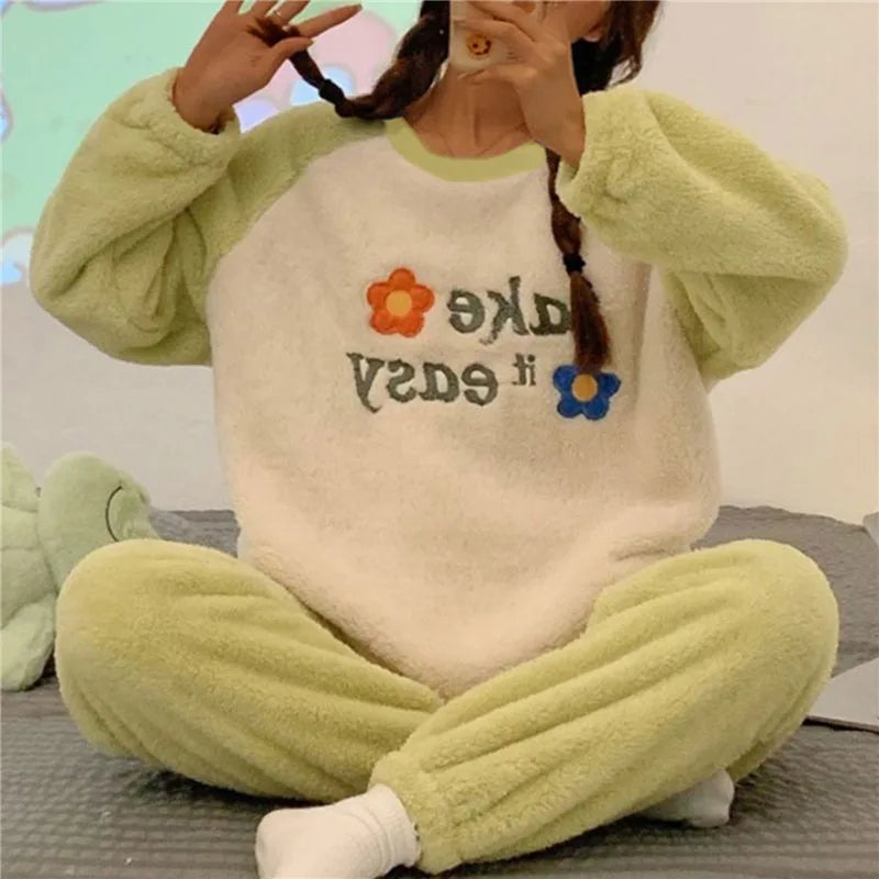 Femme portant un pyjama chaud deux tons avec manches et pantalon vert clair, et un haut blanc orné de fleurs colorées et de l’inscription “Take it easy”. Ensemble douillet, confortable et parfait pour les moments de détente à la maison.