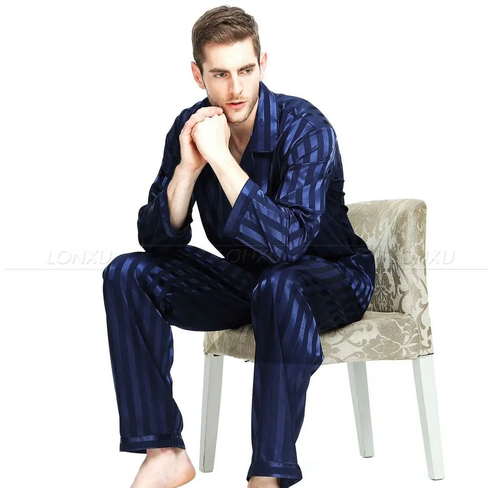 Pyjama homme Adrien en satin bleu foncé à rayures, avec une chemise à manches longues et un pantalon assorti. Le modèle est assis sur une chaise, adoptant une pose élégante et détendue, illustrant le confort et le style raffiné de ce pyjama parfait pour la nuit.