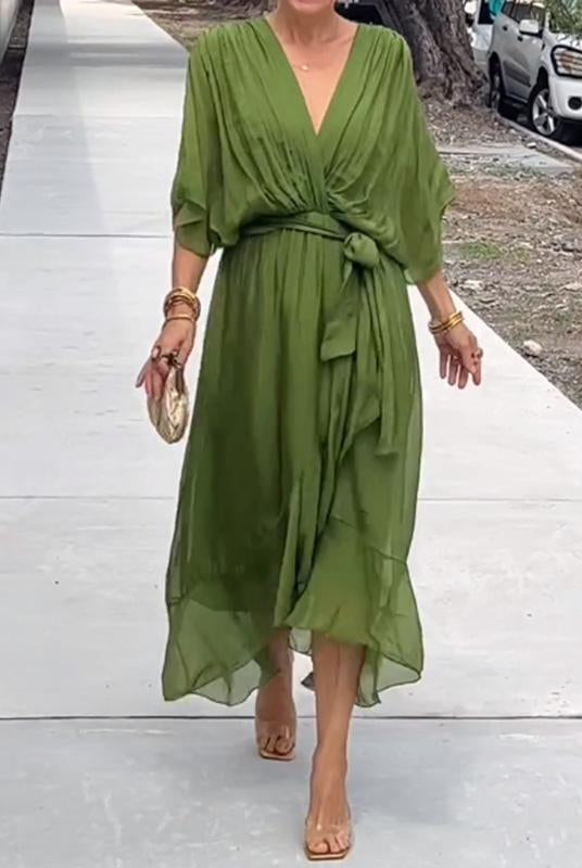 Femme portant une robe longue en chiffon vert olive, cintrée à la taille avec un nœud, et accompagnée d'un sac à main doré et des bracelets dorés.