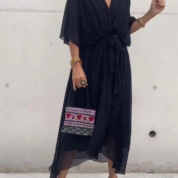 Femme portant une robe noire en chiffon fluide, avec une taille cintrée et un décolleté en V, accompagnée d'un sac à main coloré et des accessoires dorés.