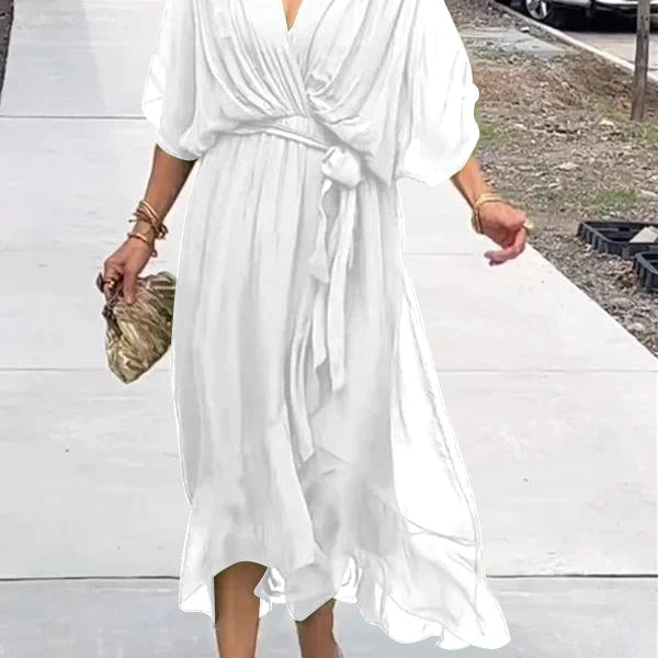 Femme marchant dans une robe chiffon blanche, avec des manches larges et une ceinture assortie, portant une pochette dorée et des sandales transparentes.