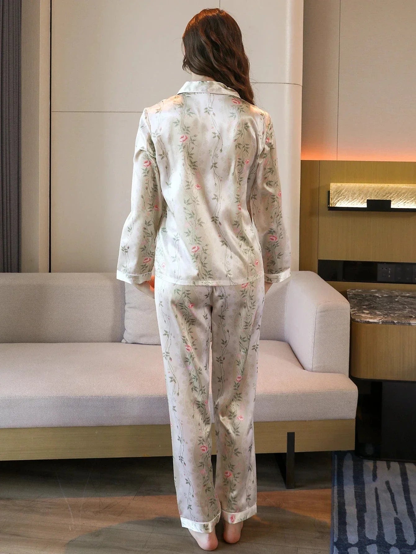 Pyjama en satin pour femme, décoré de motifs floraux délicats dans des tons de rose sur fond crème. Sur cette photo, une femme porte le pyjama vu de dos, mettant en valeur le col élégant de la chemise et les détails du pantalon. Ce pyjama est parfait pour une détente chic et confortable à la maison, alliant douceur et raffinement.