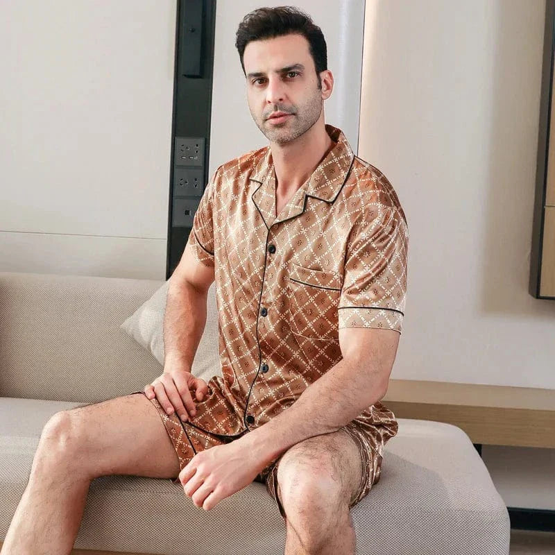 Homme assis portant le pyjama court satin Bernard pour homme, ensemble deux pièces avec chemise boutonnée à manches courtes et short assorti, motif géométrique marron, vue de face, présenté en intérieur.