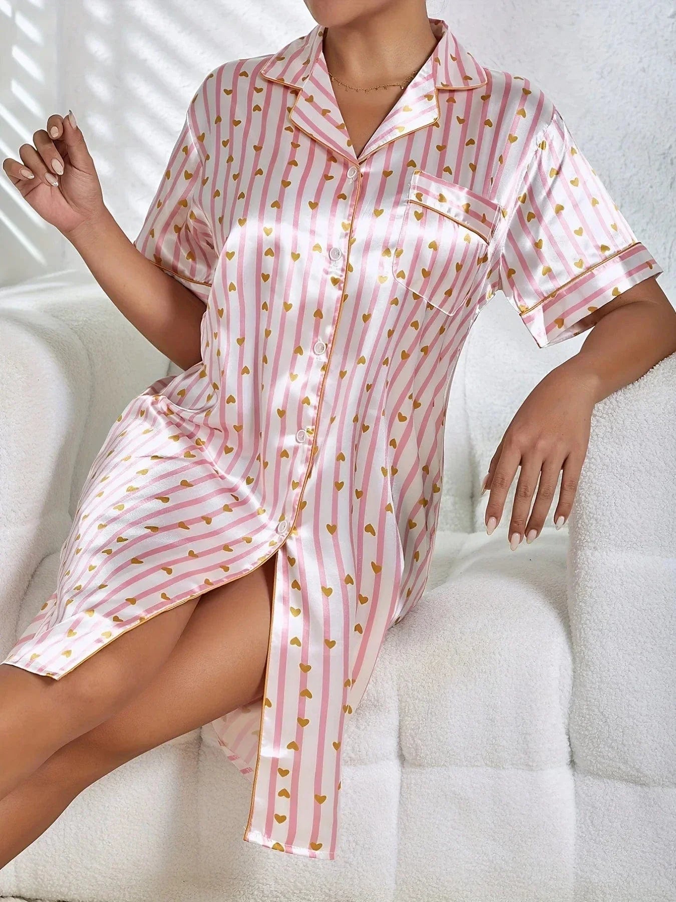 La nuisette satinée pour femme, vue de côté, avec des rayures roses et or décorées de cœurs. Le col classique et la poche sur la poitrine ajoutent une touche de style, tandis que la coupe fluide et les boutons visibles jusqu'à mi-hauteur assurent confort et élégance. Idéale pour des moments de détente dans un vêtement chic et confortable.