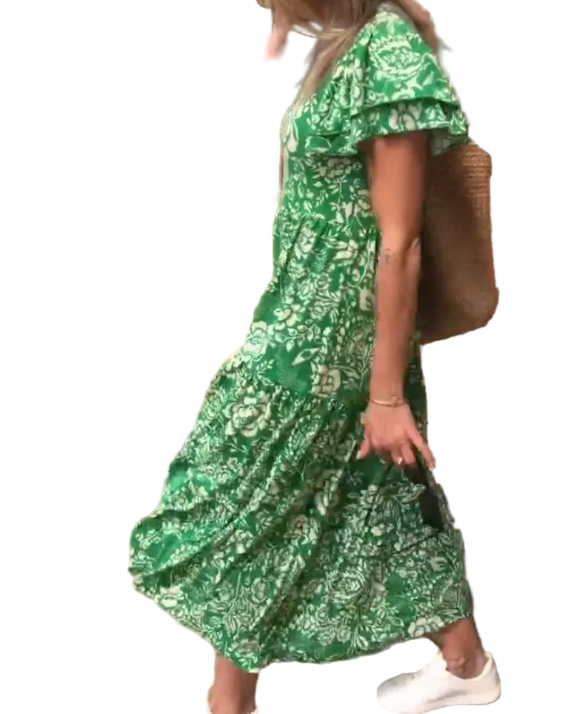 Femme marchant en robe verte à fleurs, associée à un sac en osier et des baskets blanches, dans un cadre extérieur lumineux.