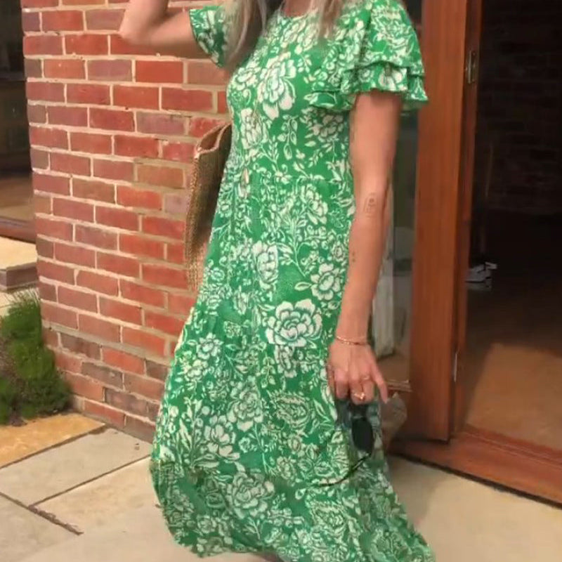 Femme souriante portant une robe verte à fleurs, avec un sac en osier et des baskets blanches, dans une ambiance extérieure ensoleillée.