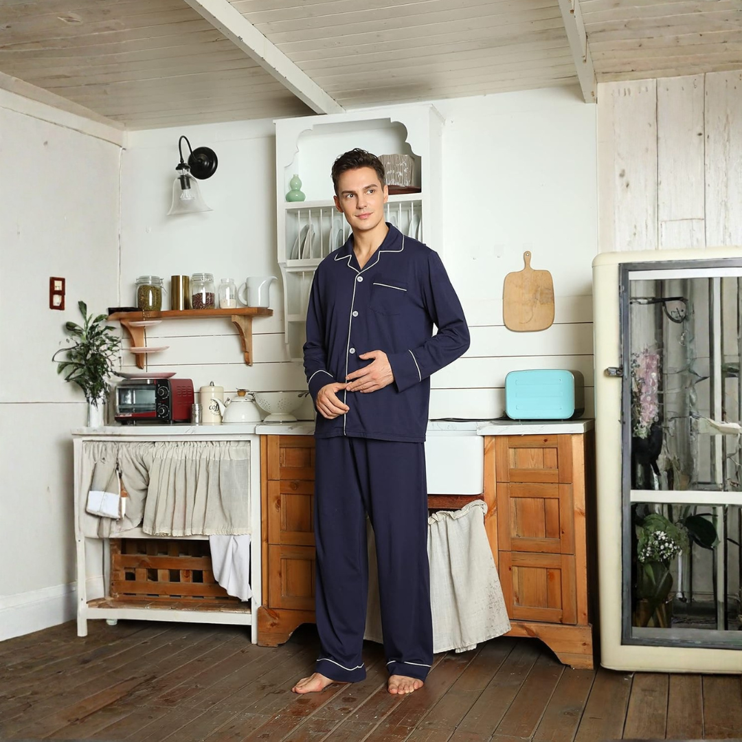 Homme debout dans une cuisine rustique, vêtu d’un pyjama bleu marine élégant avec boutons, passepoils contrastants et pantalon assorti. Ensemble confortable et raffiné, idéal pour les moments de détente à la maison ou les matinées tranquilles.