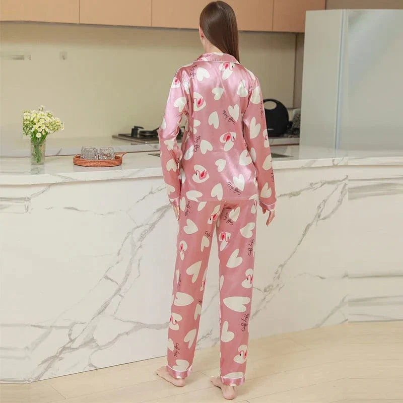Vue arrière d'une femme portant un pyjama en satin rose à motifs cœurs blancs et texte “Café Latte”. Ensemble deux pièces avec haut à col chemise et pantalon fluide. Pyjama élégant et agréable à porter, parfait pour un look cocooning moderne et féminin.