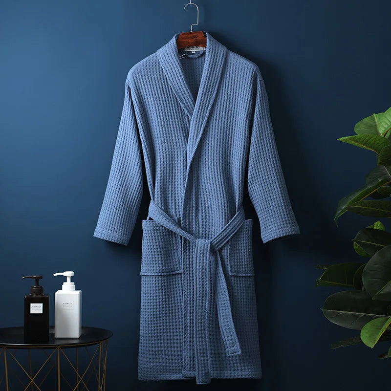 Peignoir Damien pour homme, modèle moelleux et confortable en tissu gaufré bleu, présenté suspendu devant un mur bleu avec accessoires de salle de bain en décor.