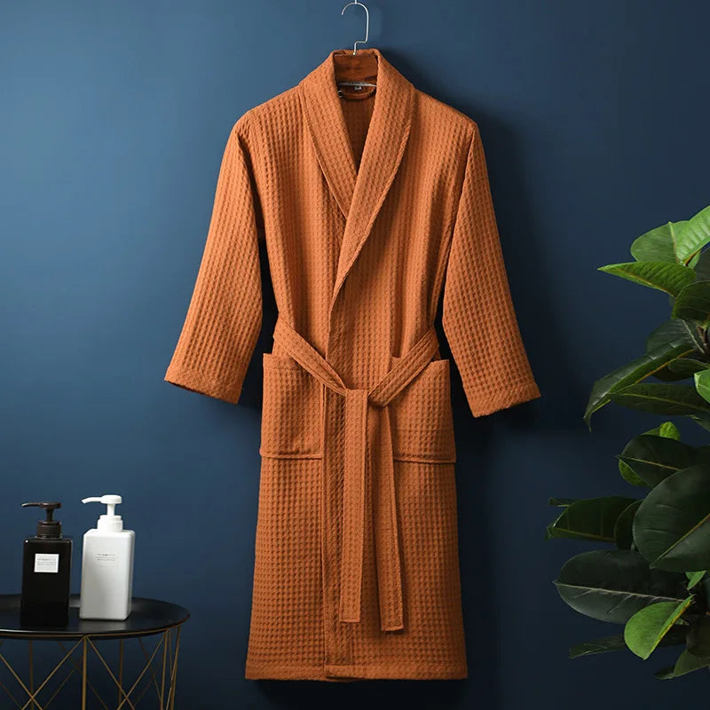 Peignoir Damien pour homme, modèle moelleux et confortable en tissu gaufré orange, présenté suspendu devant un mur bleu avec accessoires de salle de bain en décor.