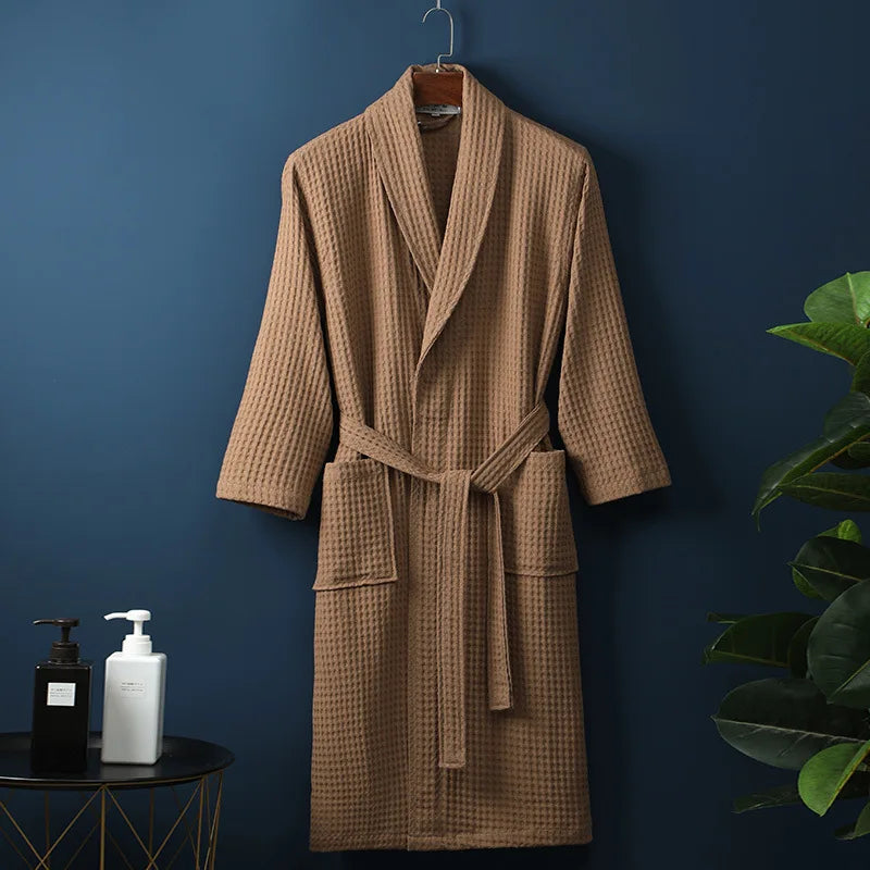 Peignoir Damien pour homme, modèle moelleux et confortable en tissu gaufré marron, présenté suspendu devant un mur bleu avec accessoires de salle de bain en décor.