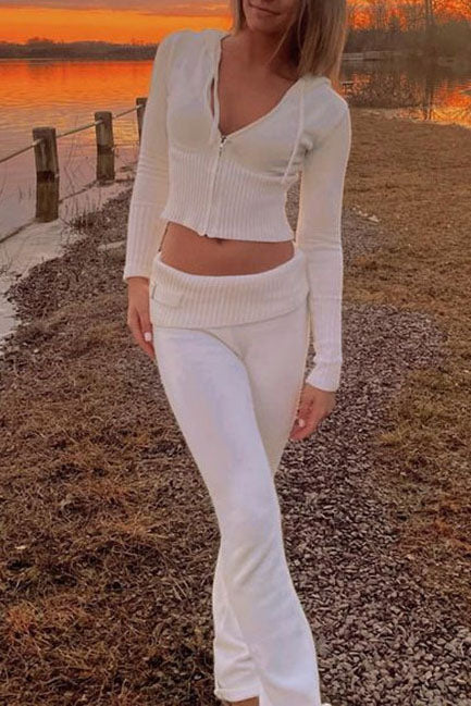 Femme marchant au bord d’un lac au coucher du soleil, vêtue de l’ensemble Dani en maille blanche, composé d’un haut zippé à manches longues et d’un pantalon taille basse assorti. Tenue douce, féminine et élégante, idéale pour un look raffiné et confortable en extérieur.