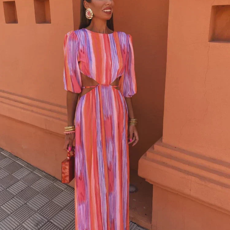 Modèle porteur de la robe maxi tie-dye pour femme, mettant en valeur le design coloré avec des teintes vibrantes de rose, violet et orange. Les manches bouffantes et les découpes latérales ajoutent une touche de modernité et de fraîcheur, idéale pour les journées estivales.