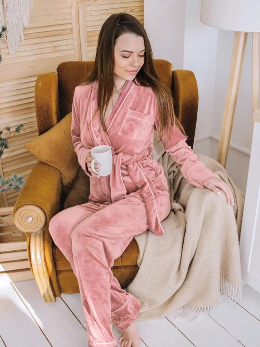 Femme assise dans un fauteuil, vêtue du pyjama Elysia en velours rose, composé d’une veste croisée ceinturée et d’un pantalon assorti. Ensemble chaud, doux et très confortable, parfait pour se détendre à la maison.