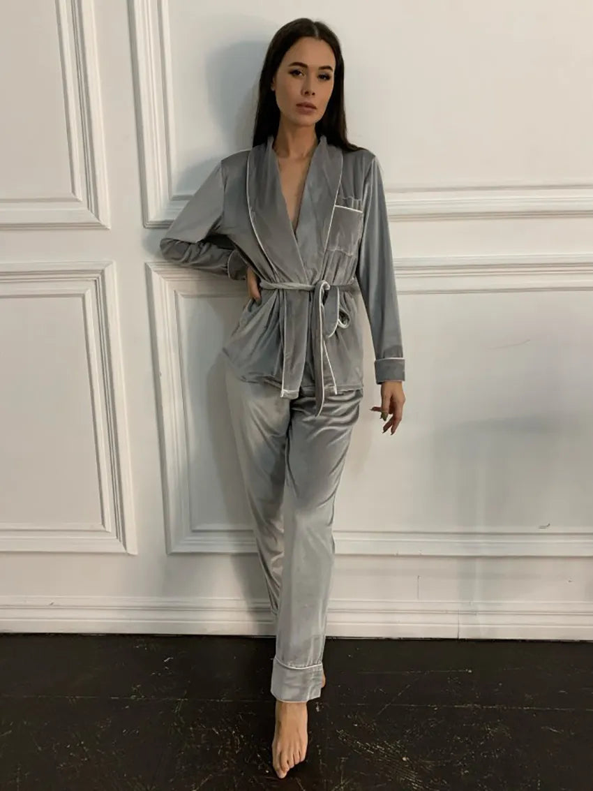 Femme portant un pyjama en velours gris composé d’une veste croisée à ceinture et d’un pantalon assorti. Ensemble chaud, doux et très confortable, idéal pour les soirées d’hiver et la détente à la maison.