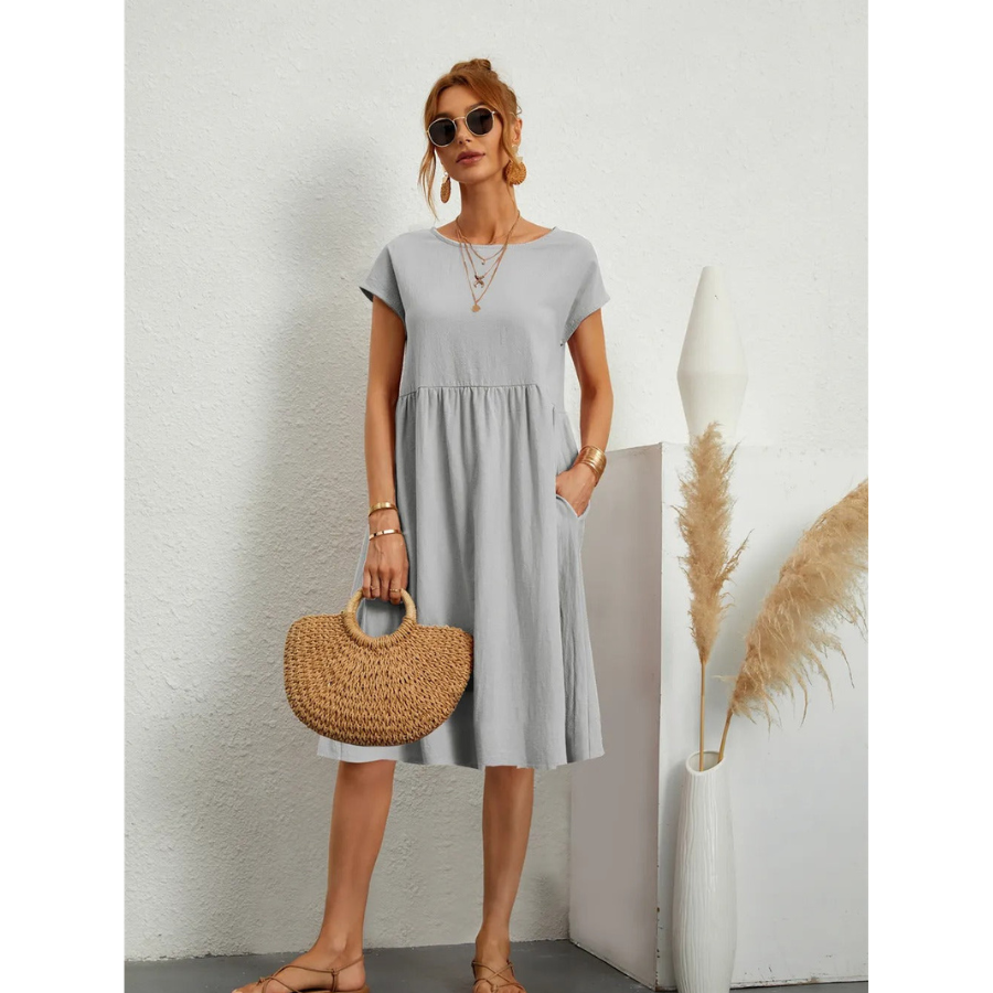 Élégante et confortable. Cette robe grise à manches courtes, avec une coupe évasée et des poches latérales, offre un style à la fois simple et chic. Accessoirisée avec un sac en osier, elle est idéale pour un look décontracté et élégant pendant les journées estivales.
