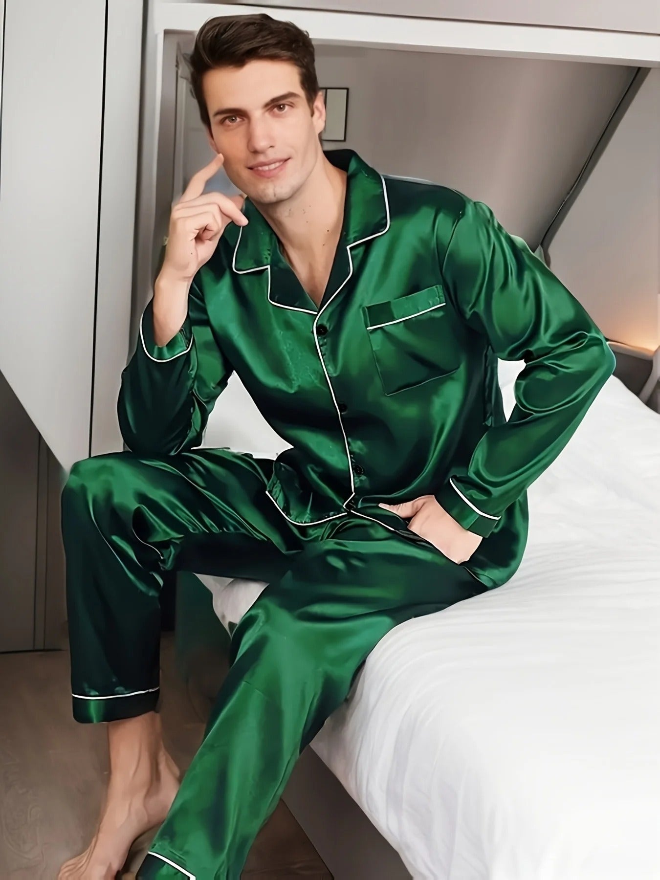 Homme assis sur le bord d’un lit, portant un pyjama long en satin vert émeraude, composé d’une chemise boutonnée avec col à passepoils contrastés et d’un pantalon assorti. Ensemble raffiné, doux et confortable, idéal pour des nuits élégantes et relaxantes.