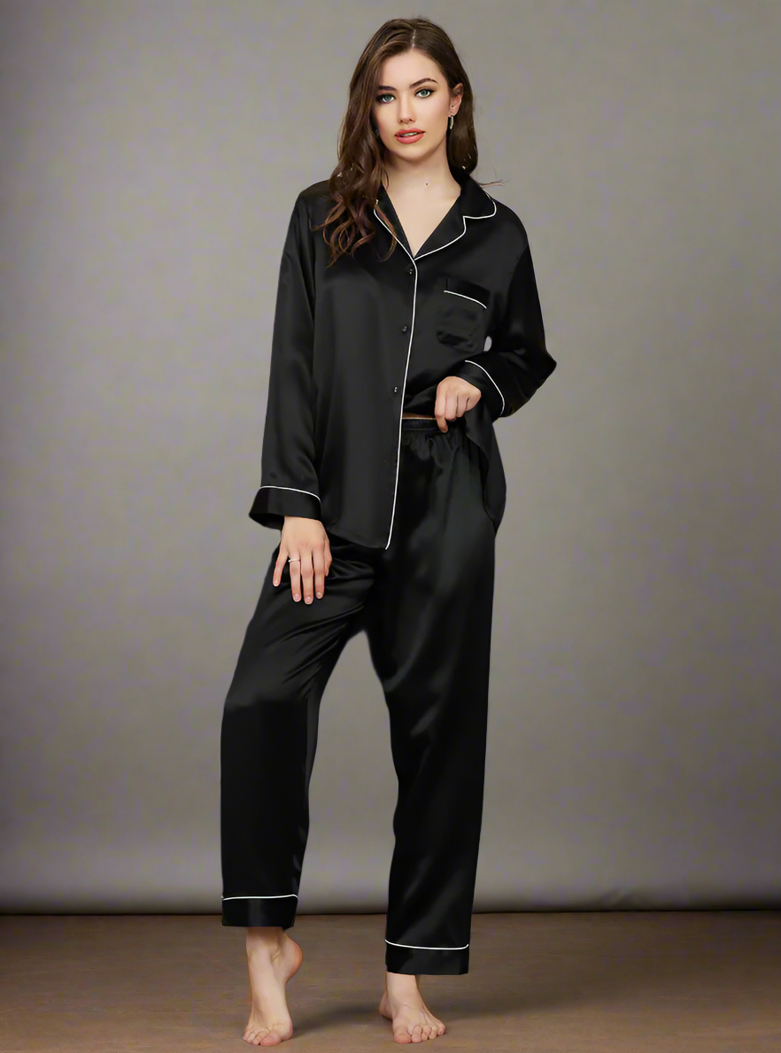 Femme debout portant le pyjama Felicity en satin noir avec passepoils blancs. Ensemble deux pièces chic et fluide, à la fois doux et élégant, idéal pour des nuits raffinées ou des moments de détente avec style.