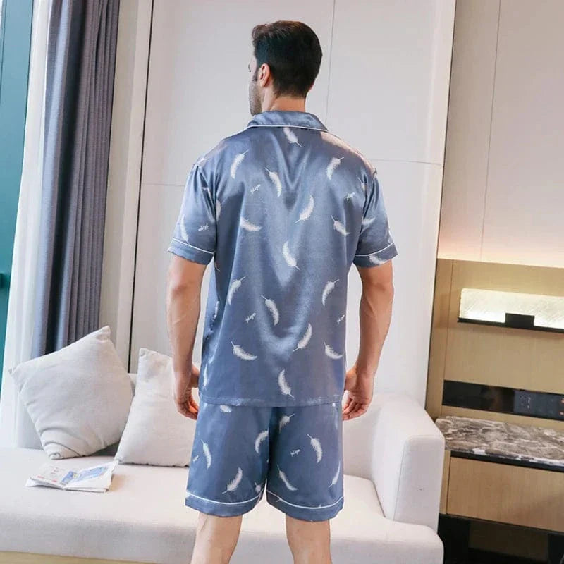 Vue arrière d’un homme portant le shorty satin Gabriel pour homme, ensemble deux pièces avec chemise à manches courtes et short assorti, motif plume clair sur fond bleu, coupe droite, présenté en intérieur.