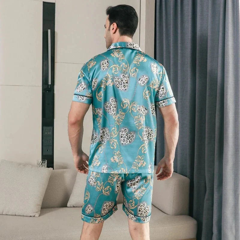 Vue arrière d’un homme portant le pyjama satin Georges pour homme, ensemble deux pièces avec chemise à manches courtes et short assorti, imprimé décoratif vert turquoise, coupe droite, présenté en intérieur.
