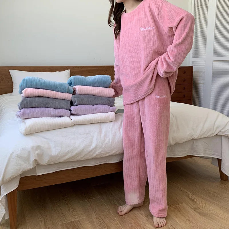 Femme portant un pyjama rose en tissu côtelé, composé d’un haut à manches longues et d’un pantalon assorti. Ensemble doux et confortable, parfait pour la maison. Plusieurs autres coloris du même modèle sont empilés sur un lit en arrière-plan.