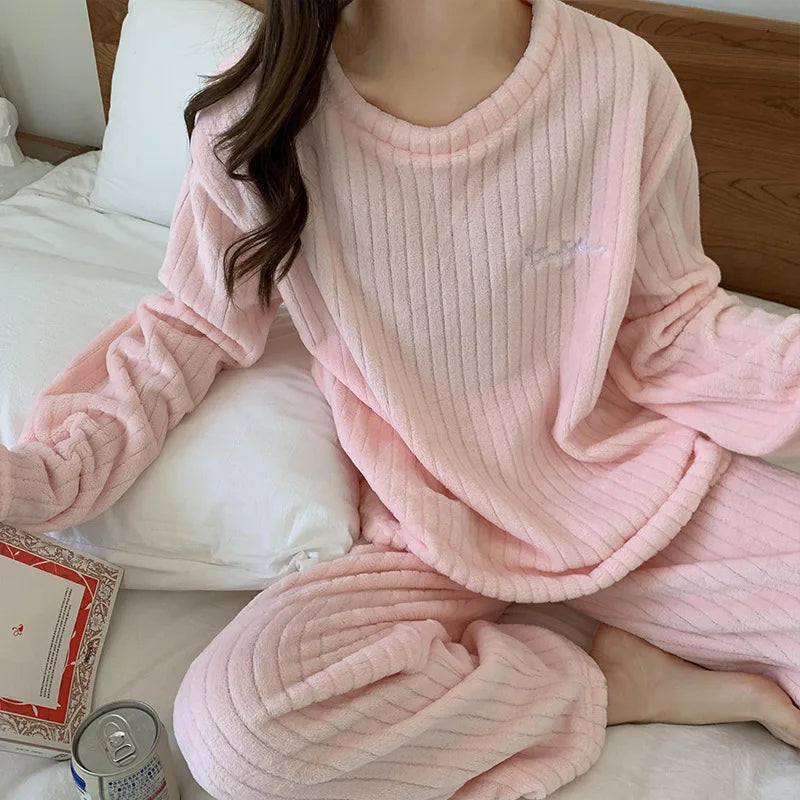 Femme assise sur un lit portant un pyjama rose pâle en tissu côtelé, avec haut à manches longues et pantalon assorti. Ensemble ultra doux et confortable, idéal pour se détendre ou lire à la maison.