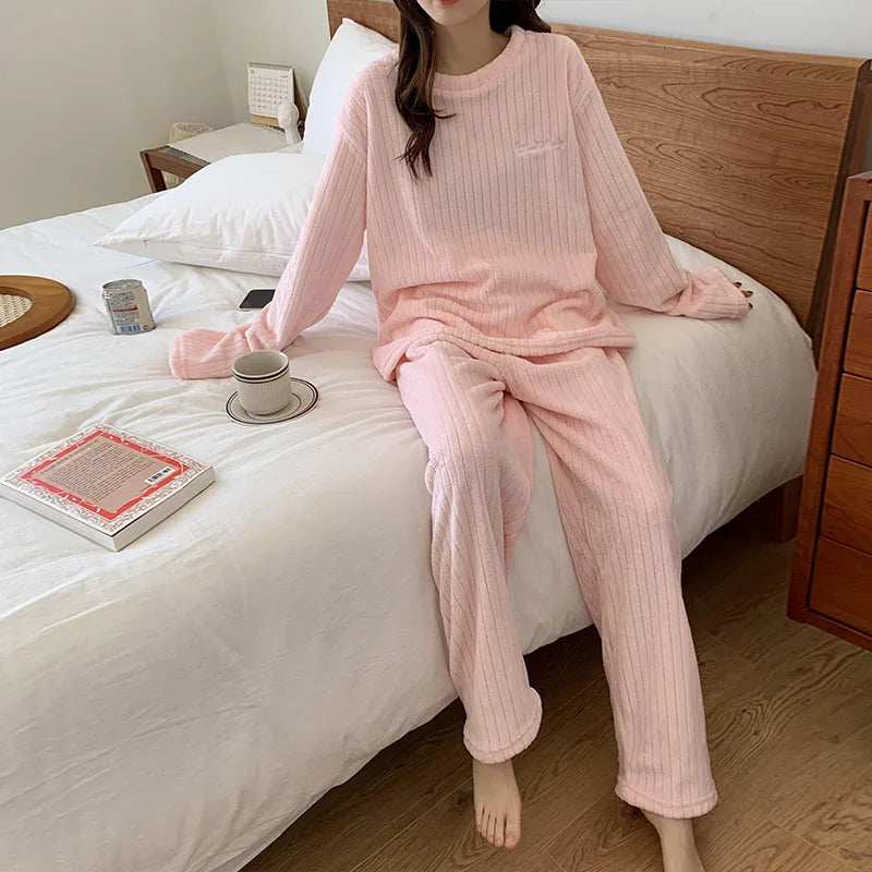Femme assise sur un lit portant un pyjama rose clair en tissu côtelé, composé d’un haut à manches longues et d’un pantalon assorti. Ensemble doux, confortable et parfait pour les moments cocooning à la maison.