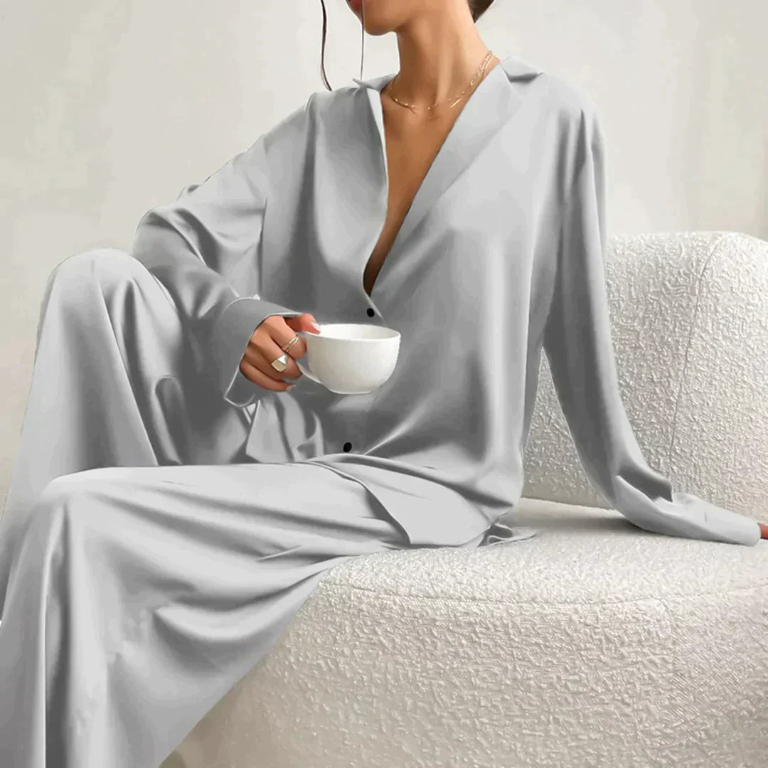 Femme portant le pyjama en coloris gris clair, un ensemble raffiné avec chemise fluide à col ouvert et pantalon ample. Tenue douce, élégante et confortable, idéale pour la nuit et les moments de détente.