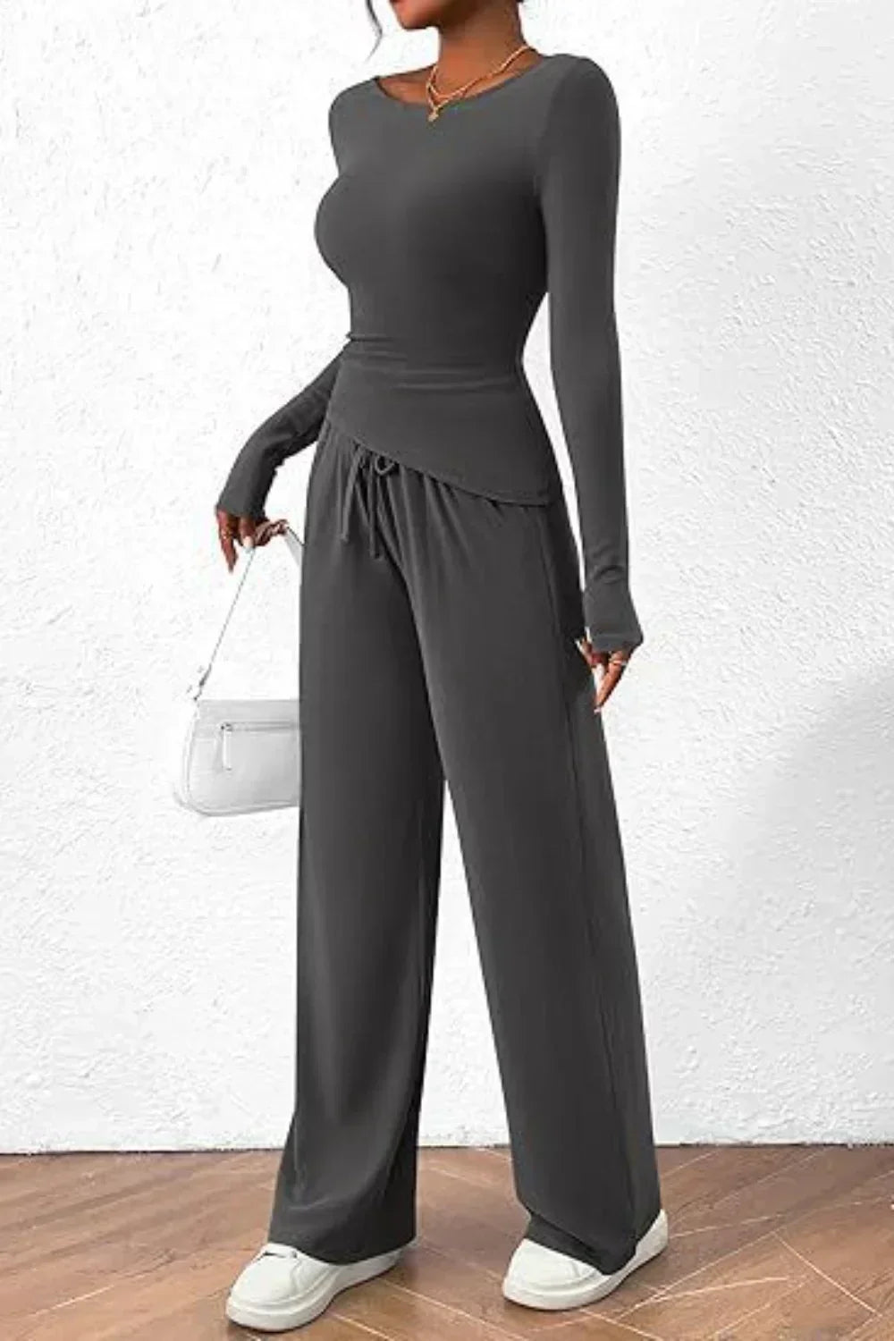 Femme portant un ensemble lounge gris anthracite, composé d’un haut à manches longues ajusté et d’un pantalon large à cordon et poches. Tenue douce, confortable et élégante, parfaite pour un look décontracté ou une journée détente chic.