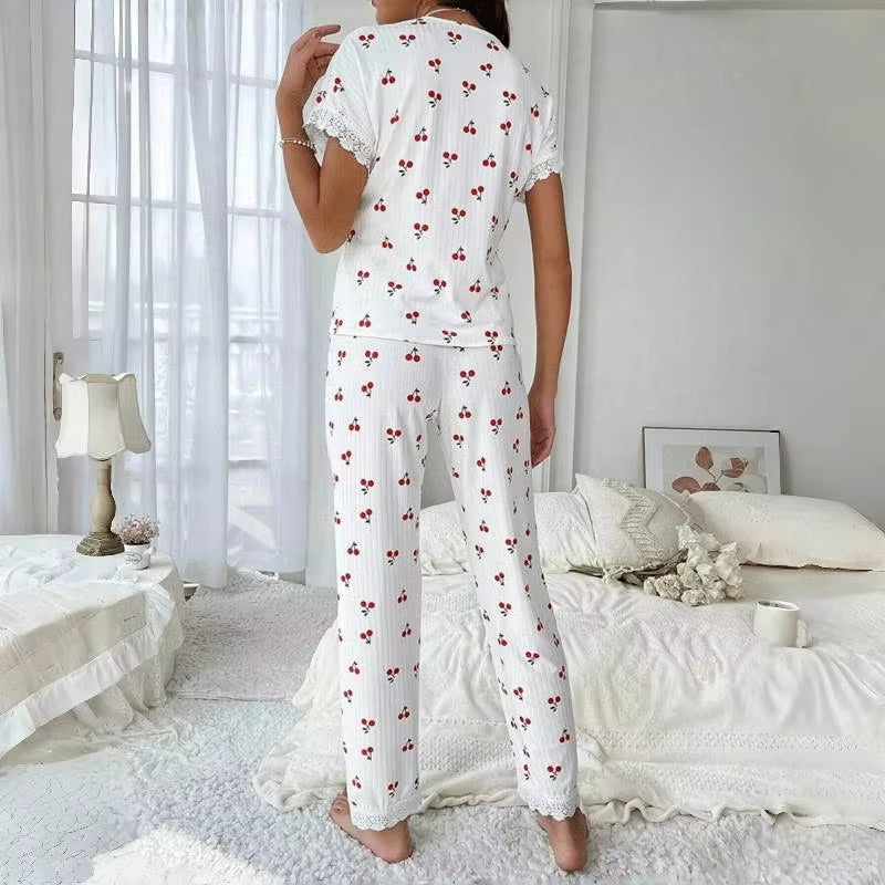 Vue arrière d’un pyjama femme blanc à motifs cerises rouges, composé d’un haut à manches courtes et d’un pantalon long, avec détails en dentelle blanche aux manches et aux chevilles. Ensemble léger, confortable et idéal pour les nuits d'été ou les matins cocooning.