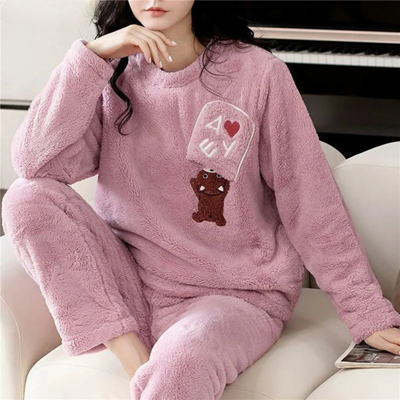Femme portant un pyjama moelleux rose mauve composé d’un haut à manches longues orné d’un motif ourson brodé avec des lettres et d’un pantalon assorti. Ensemble doux, chaud et relaxant, idéal pour les soirées cocooning à la maison.