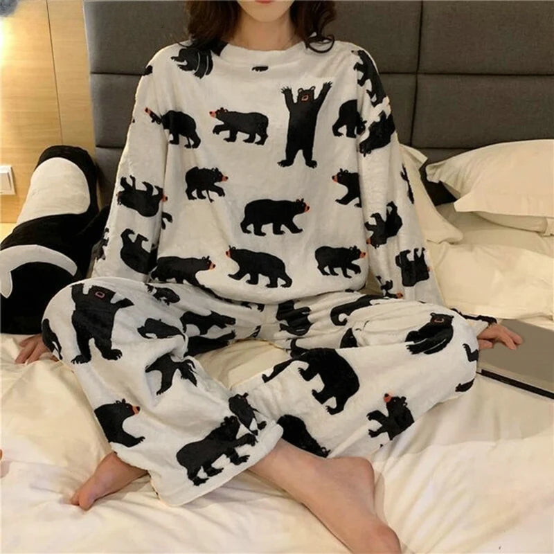 Femme portant un pyjama moelleux blanc imprimé de petits ours noirs dans différentes positions. Ensemble à manches longues avec pantalon assorti, doux, chaud et relaxant, parfait pour les soirées cocooning à la maison.