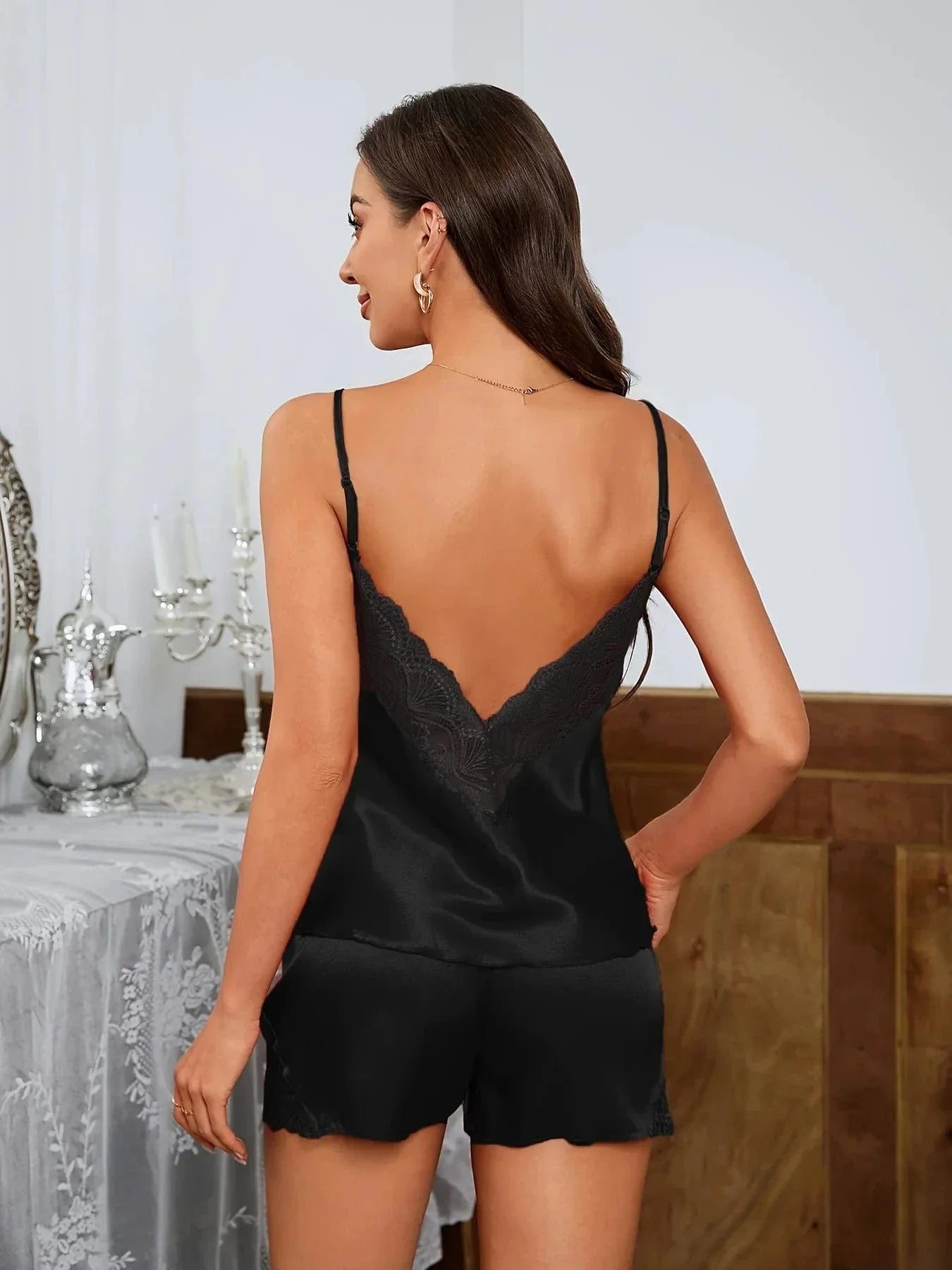 Femme vue de dos portant un pyjama deux pièces en satin noir, composé d’un débardeur à fines bretelles avec dos en V orné de dentelle et d’un short fluide assorti avec finitions en dentelle. Ensemble léger, élégant et confortable, parfait pour les nuits estivales ou les moments de détente à la maison.