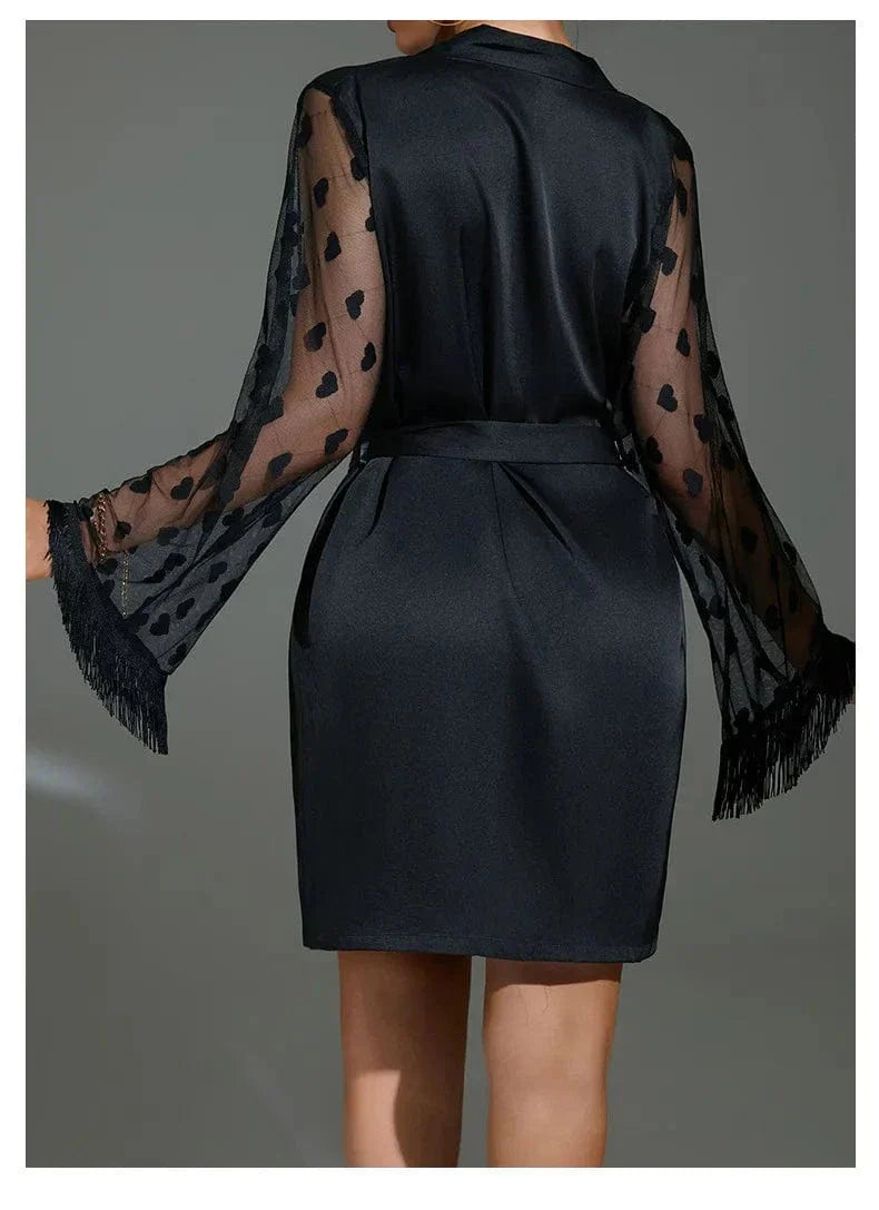 Vue de dos du peignoir Lucie en satin noir, avec manches longues transparentes décorées de cœurs et finitions à franges. Ceinture à nouer à la taille. Lingerie élégante et séduisante, idéale pour une touche glamour et féminine à la maison.