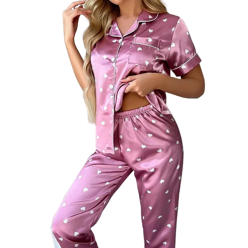 Femme portant le pyjama Pyjama femme Doux, élégant & agréable , un ensemble satiné rose décoré de petits cœurs blancs, composé d’une chemise à manches courtes et d’un pantalon fluide, offrant confort et douceur pour la nuit.