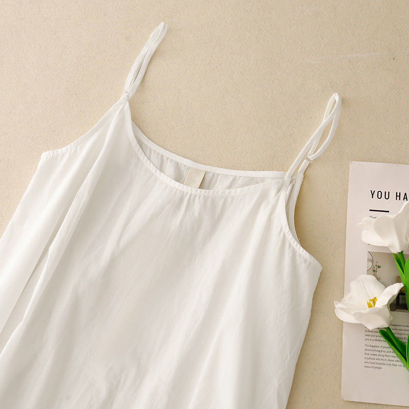 détail du haut de la nuisette blanche à fines bretelles avec encolure arrondie, présentée à plat sur fond beige.