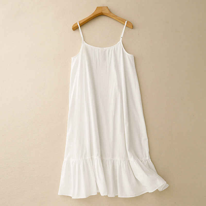 nuisette blanche fluide à fines bretelles, coupe ample avec volant au bas, suspendue sur cintre devant un mur beige.