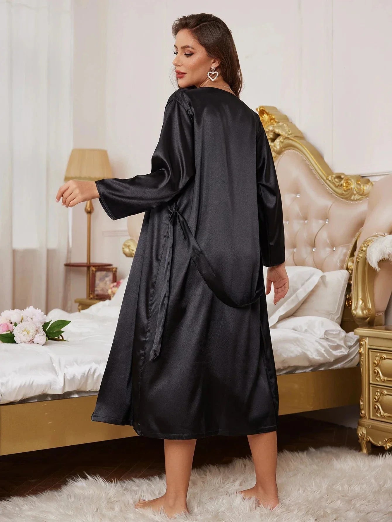 Femme de dos portant un peignoir long en satin noir, à manches longues et ceinture nouée à la taille. Lingerie élégante et fluide, idéale pour des moments de confort et de raffinement à la maison.