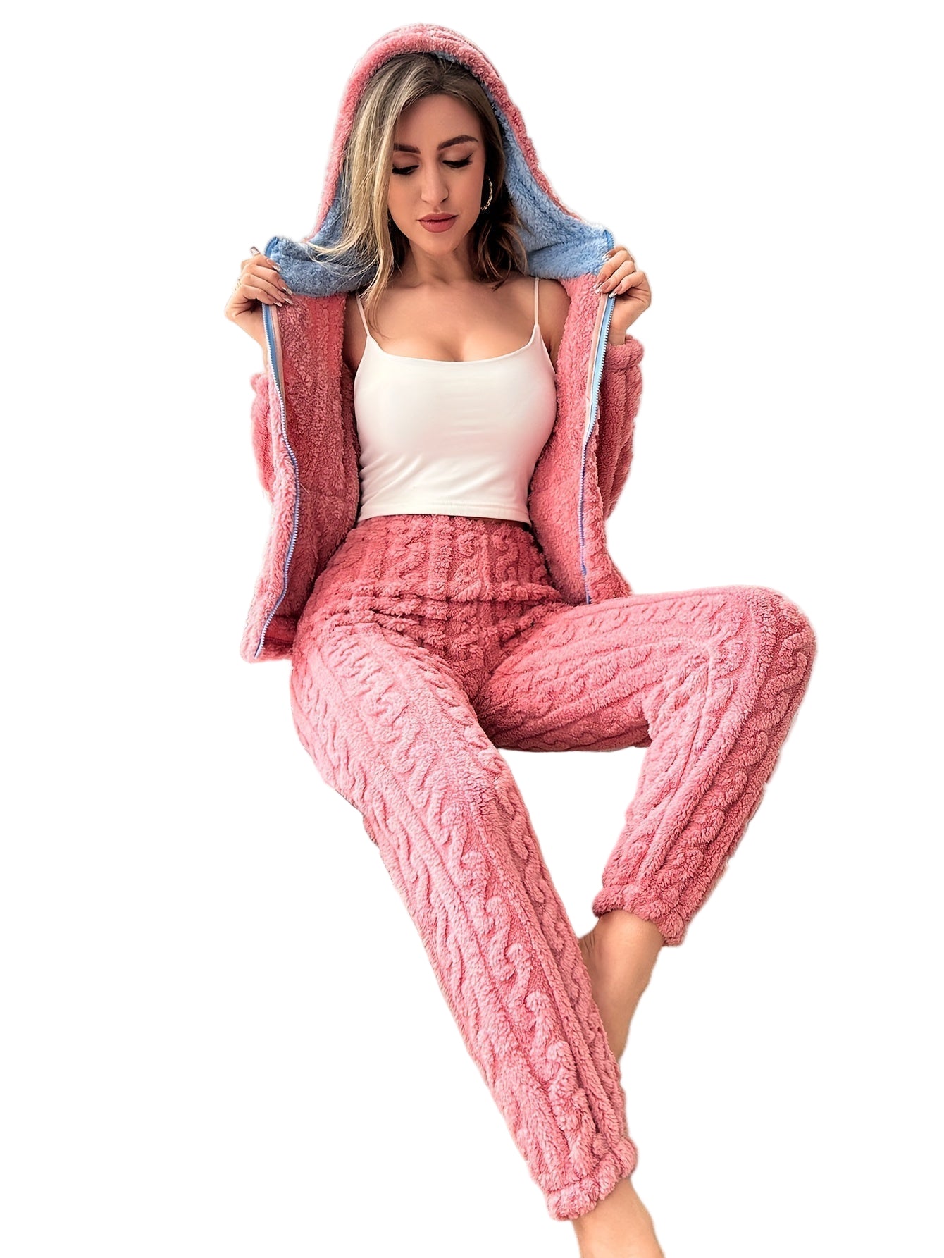 Femme portant un pyjama en maille polaire rose avec capuche doublée bleue, composé d’un pantalon chaud à motifs torsadés et d’une veste zippée, parfait pour rester stylée et au chaud à la maison.