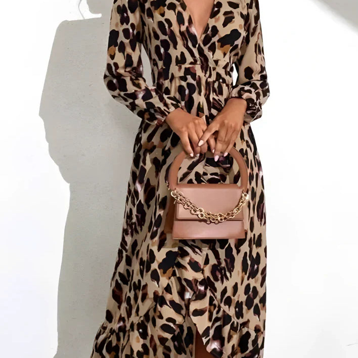 Femme portant une robe léopard à manches longues et fente sur le côté, avec un sac à main beige, devant un fond blanc.