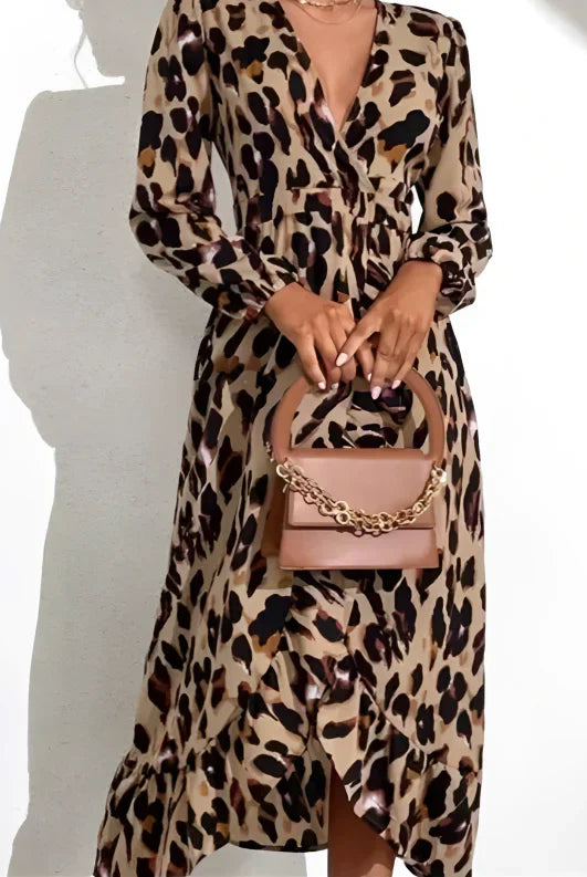 Femme portant une robe léopard à manches longues et fente sur le côté, avec un sac à main beige, devant un fond blanc.