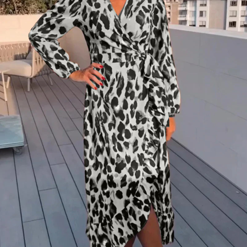 Femme portant une robe longue à imprimé léopard noir et blanc, avec une coupe croisée, une fente sur le côté et un détail de ceinture, créant une silhouette chic et fluide.