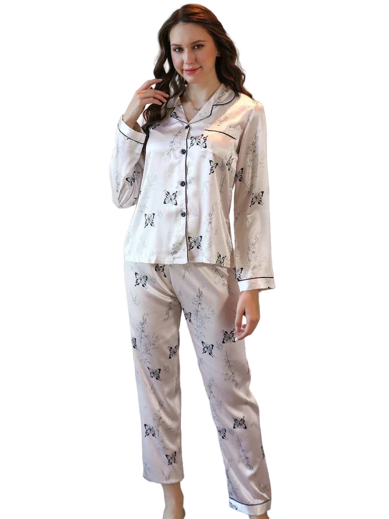 Femme souriante portant un pyjama long en satin beige clair, orné de motifs papillons noirs et de feuillage discret. Ensemble composé d’un haut boutonné à manches longues avec col passepoilé noir et d’un pantalon assorti. Pyjama élégant, fluide et agréable, parfait pour les nuits douces ou les moments de détente à la maison.