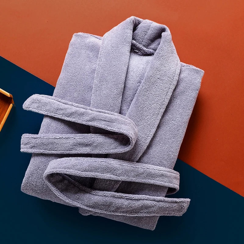 Peignoir Pascal pour homme, modèle épais et chaleureux en tissu éponge gris clair, présenté plié avec ceinture assortie sur un fond coloré moderne bleu et terracotta.