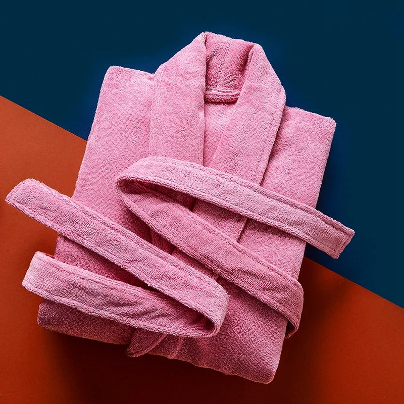 Peignoir Pascal pour homme, modèle épais et chaleureux en tissu éponge rose vif, présenté plié avec sa ceinture assortie sur un fond coloré bleu nuit et terracotta.