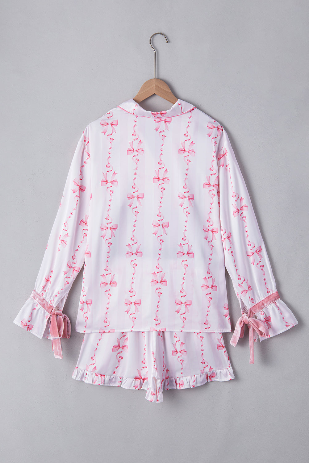 Pyjama femme Pascale blanc à motifs nœuds roses, vue de dos de l’ensemble deux pièces sur cintre avec chemise à manches longues et short assorti, finitions volantées et liens à nouer aux poignets.