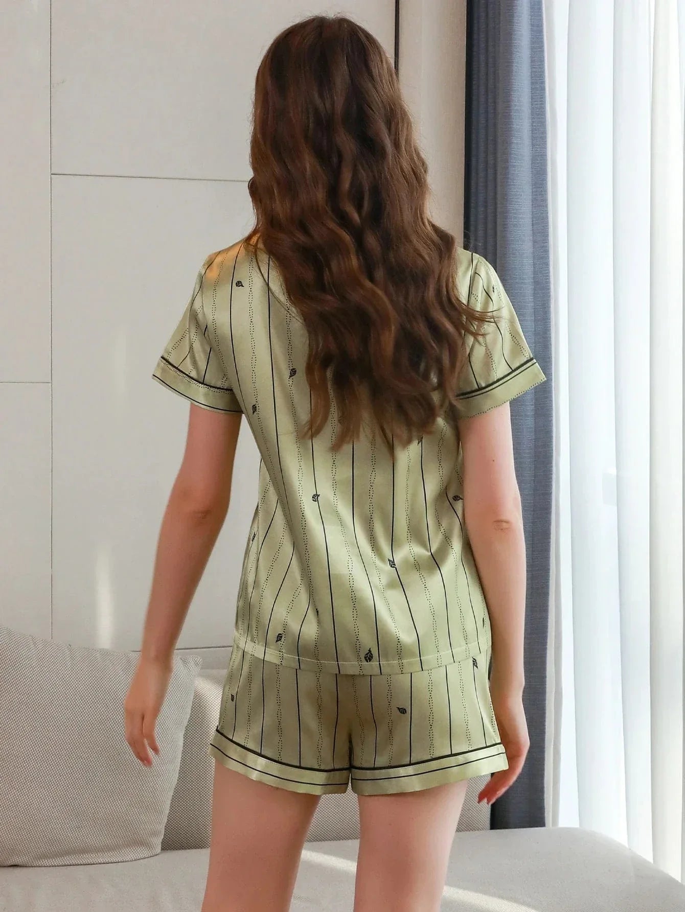 Vue de dos d’une femme portant un pyjama court en satin vert clair, orné de fines rayures noires et petits motifs. Ensemble composé d’un haut à manches courtes et d’un short assorti. Tenue légère, confortable et élégante, idéale pour les nuits d’été ou les moments de détente à la maison.