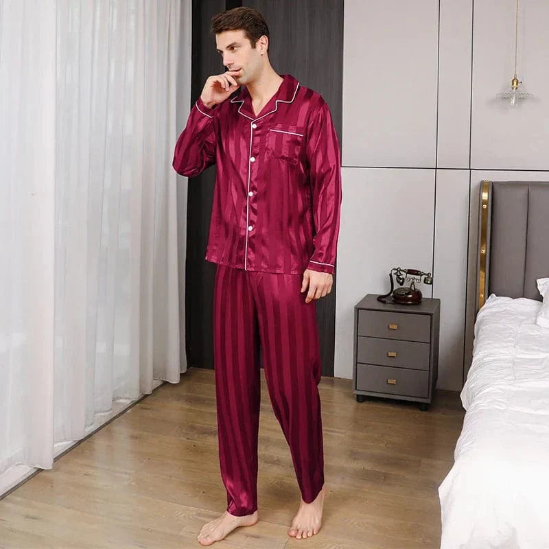 Homme debout portant le pyjama satin pour homme Philippe, ensemble léger et raffiné en satin bordeaux à fines rayures, avec chemise boutonnée à manches longues, col passepoilé et pantalon assorti, illustrant une coupe élégante et un tombé fluide idéal pour le confort nocturne.