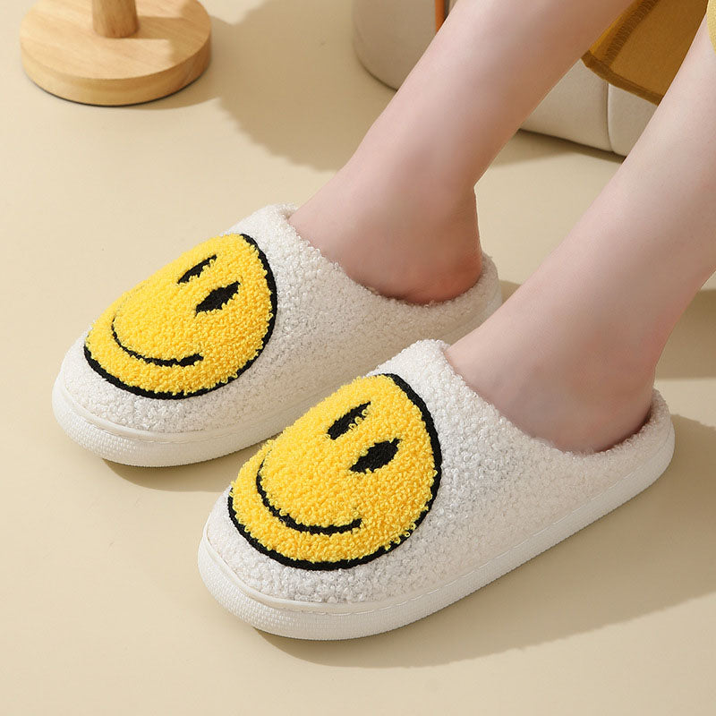 Chaussons unisexe Sasha blancs en matière pelucheuse avec grand smiley jaune, portés aux pieds, intérieur chaud et moelleux, semelle confortable pour un style cosy à la maison.